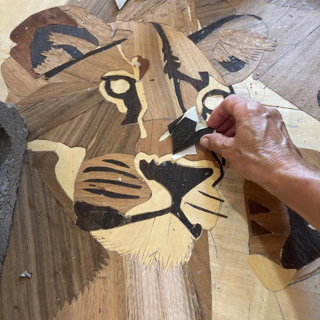 Detalle de las manos de Carina ensamblando piezas de madera en un rostro de tigre