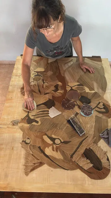 Carina lijando el mosaico de madera de un tigre en su mesa de trabajo